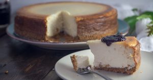 Whole cheesecake in background with big slice on a plate with a fork and some kind of berry topping | Goldstein Mtitsubishi