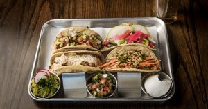 4 different kind of tacos on a tray with a beer in the background | Goldstein Chrysler Jeep Dodge RAM